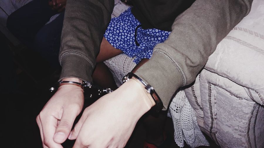 Midsection of man with handcuffs sitting on bed