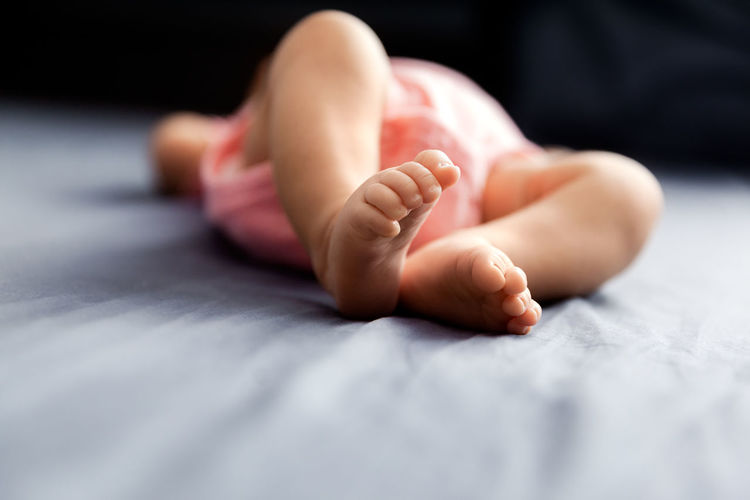Low section of baby girl lying on bed at home