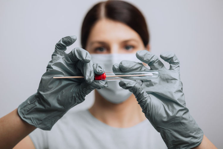 Close-up of doctor wearing mask holding test tube against gray background