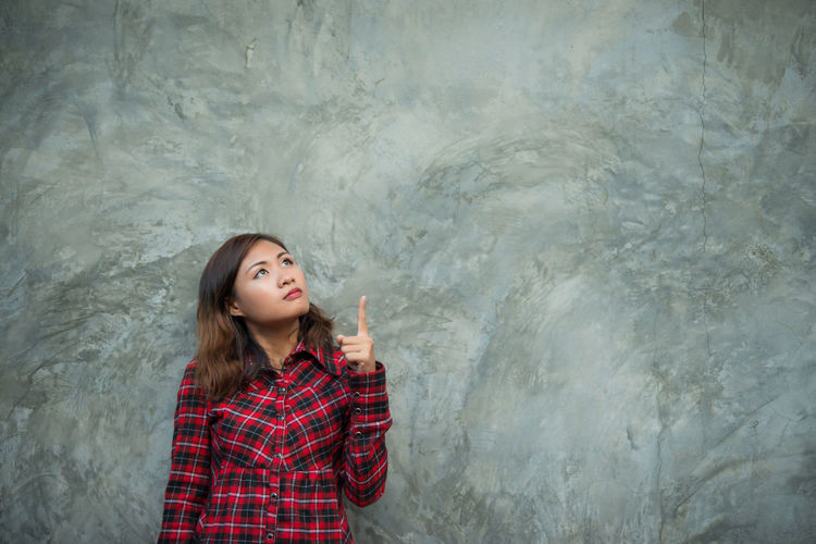 Beautiful young woman gesturing while standing against wall