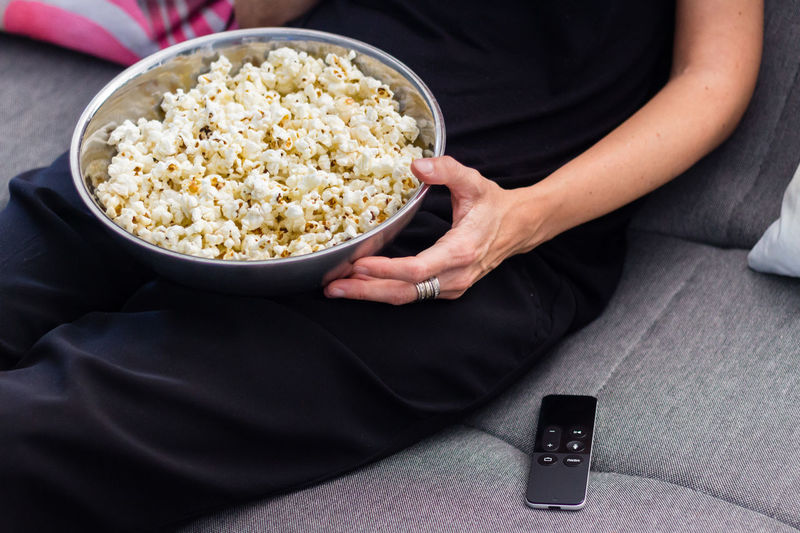 Midsection of woman with popcorns sitting on sofa at home