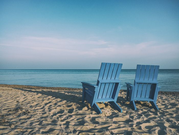 Outdoor chairs on sand against sea at beach