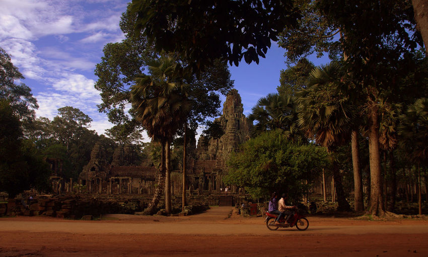 People riding motorcycle on dirt road outside historic temple