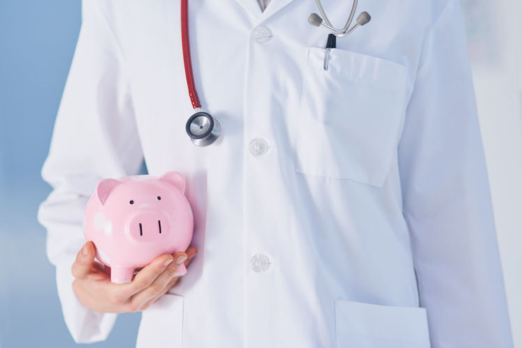 Midsection of doctor holding piggy bank