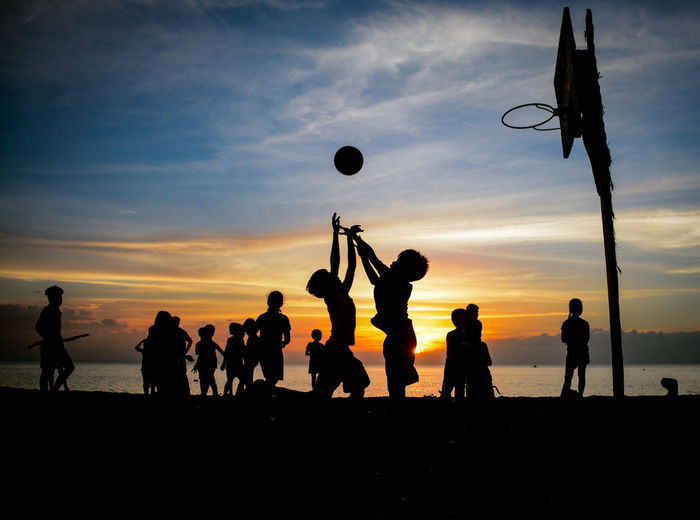 Silhouette people playing soccer on beach against sky during sunset