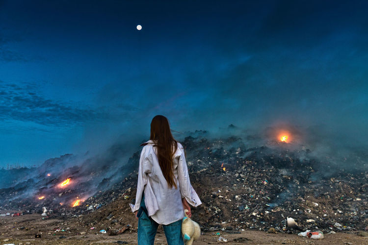 Rear view of woman standing against junkyard at night