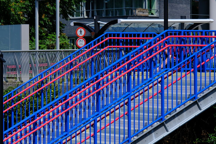 Metal fence in blue and red color against blue sky in city.  