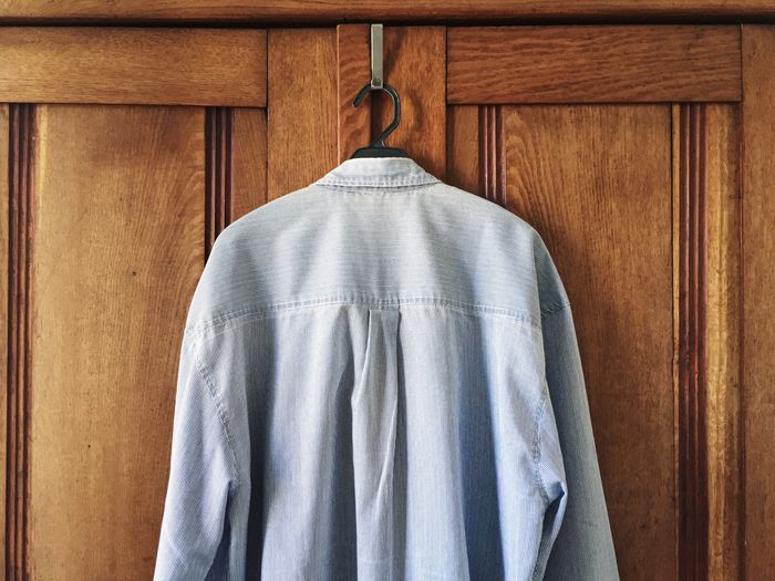 Gray shirt on coathanger hanging from wooden cabinet