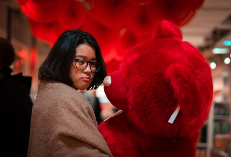 Young woman holding red teddy bear while standing in room