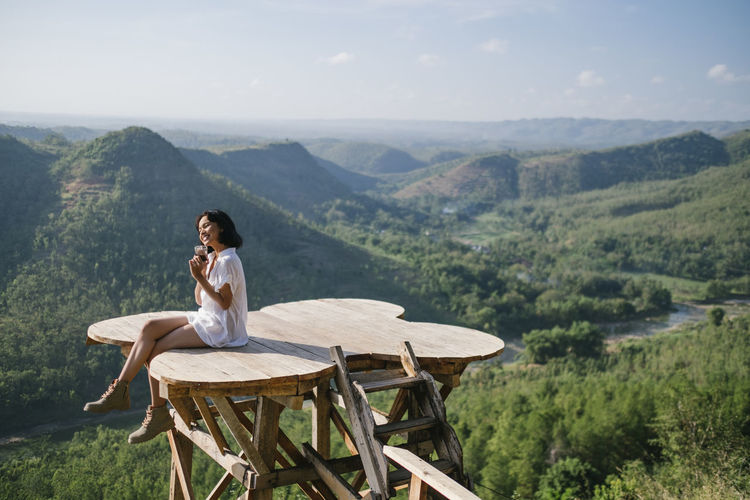 Full length of woman sitting at observation point against mountains and sky