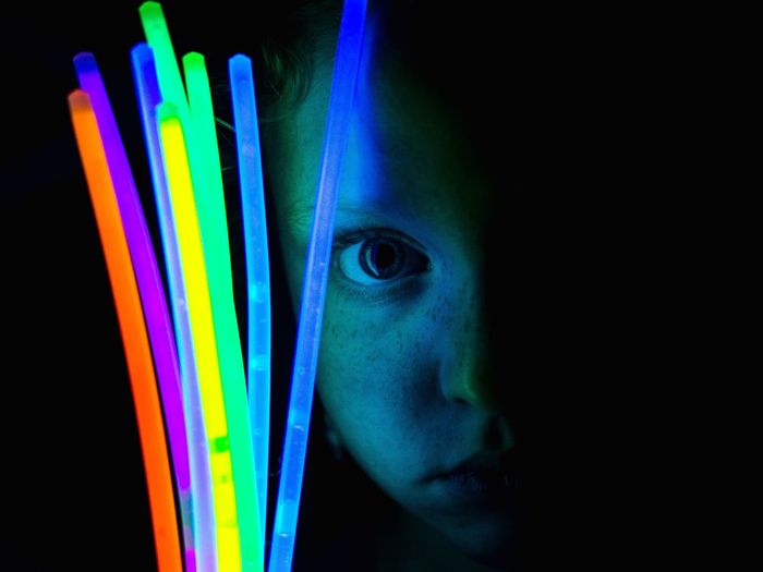 Portrait of girl holding glow sticks against black background