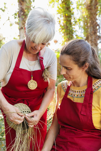 Smiling artisan showing basket making with esparto grass to coworker