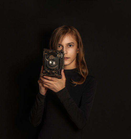 Portrait of young woman photographing against black background