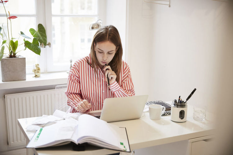 Female accountant using laptop while doing paperwork at home