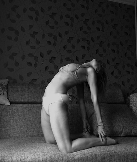 Full length of sensuous woman kneeling on sofa at home
