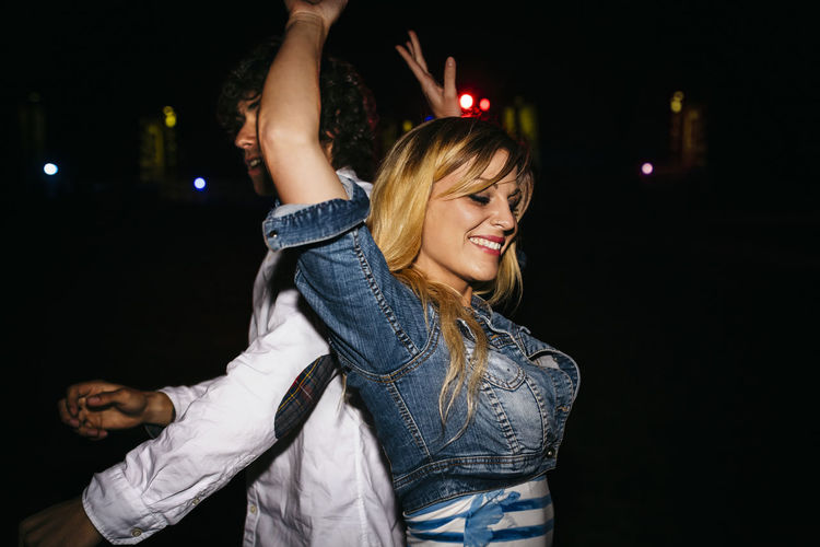 Happy young woman dancing back to back with a man at summer night festival