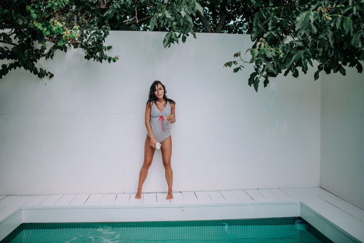 Portrait of woman standing by swimming pool against wall