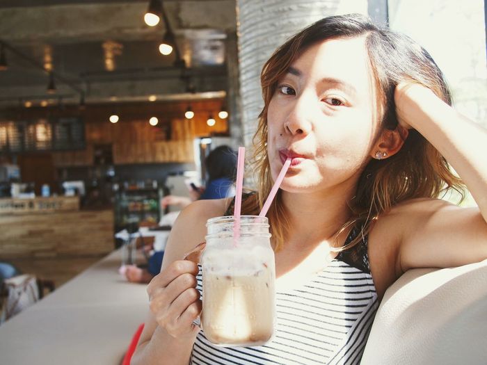 Portrait of young woman drinking iced coffee in restaurant