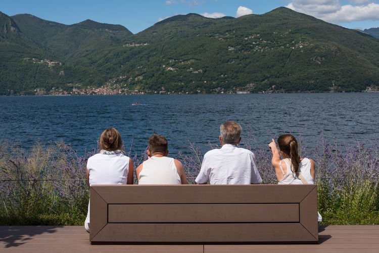Rear view of people sitting at lakeshore against mountains