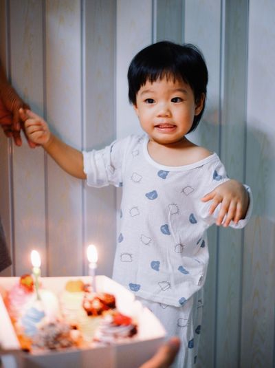 Cute boy standing by cake at home