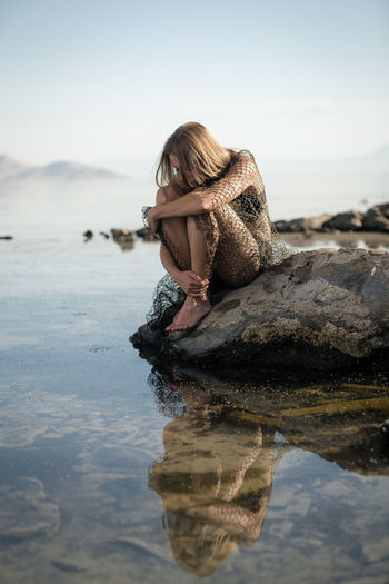 Young woman relaxing on rock in sea against clear sky
