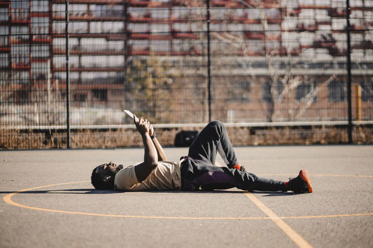 Young man using digital tablet while lying down on sports court during sunny day