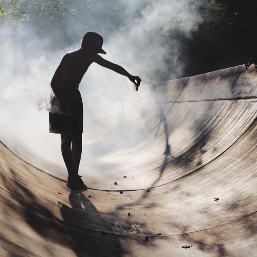 Full length of boy spreading smoke at skateboard park