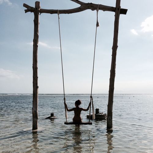 Full length rear view of woman sitting on swing over sea against sky