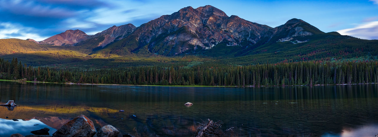 Calm lake in front of rocky mountains against blue sky