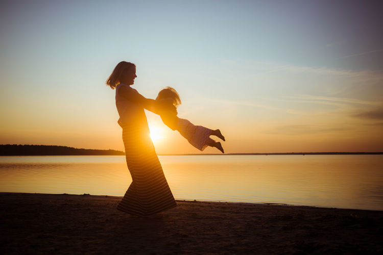 Silhouette woman playing with daughter on beach during sunset