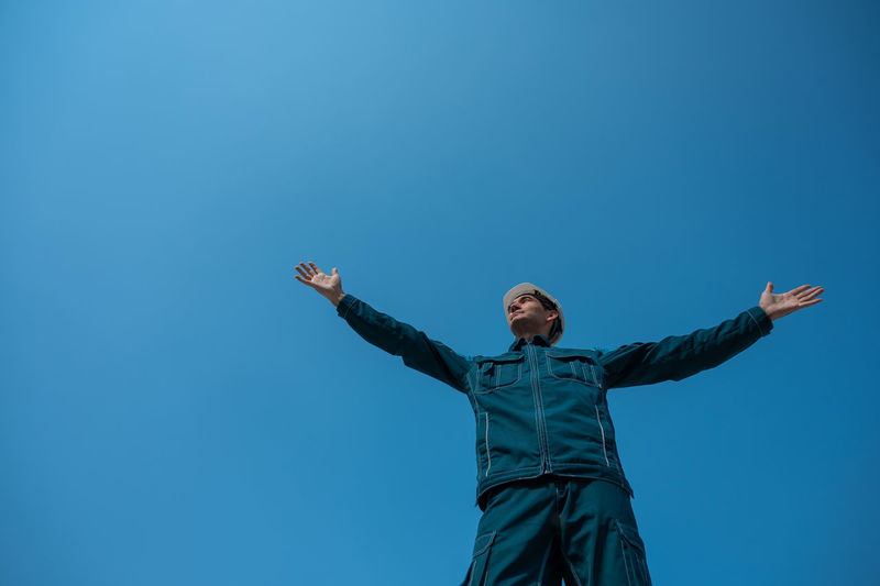 Low angle view of woman standing against clear blue sky