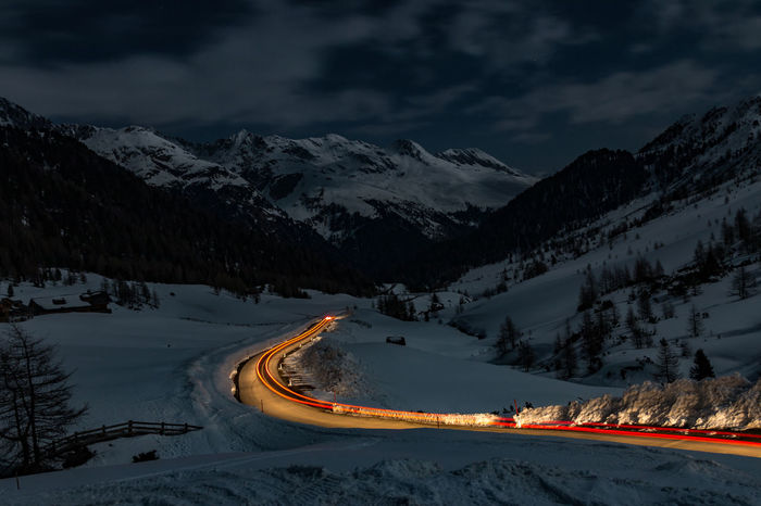 Light trails on road by snow covered field at dusk