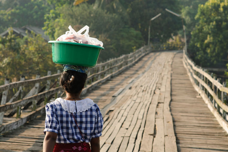 Rear view of woman carrying bucket on footbridge