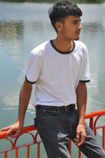 Young man looking away while standing on lake