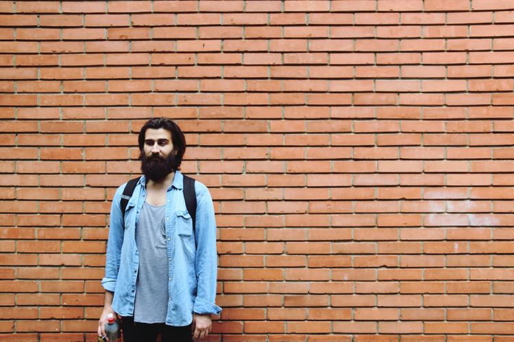 Young hipster standing against brick wall