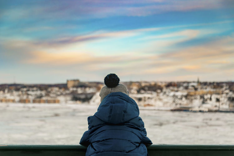 6 years old boy in winter clothes watching the sunset over the river