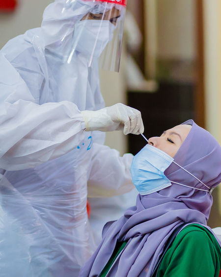 Healthcare worker with protective equipment performs nose swab for covid-19.
