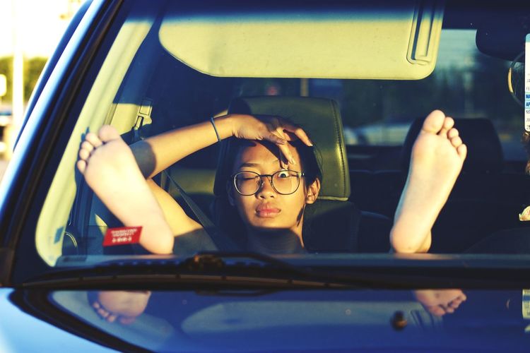 Portrait of young woman sitting with feet up in car seen through windshield