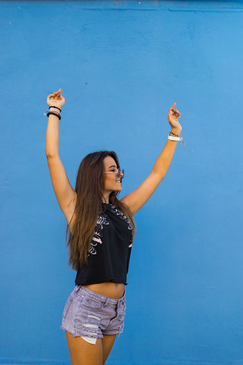 Teenage girl with arms raised standing against wall