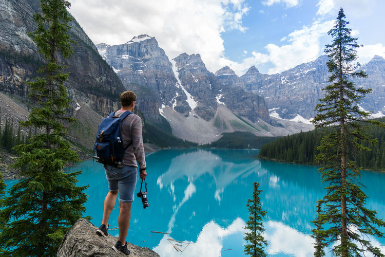 Rear view of man standing on rock while looking at mountains against sky