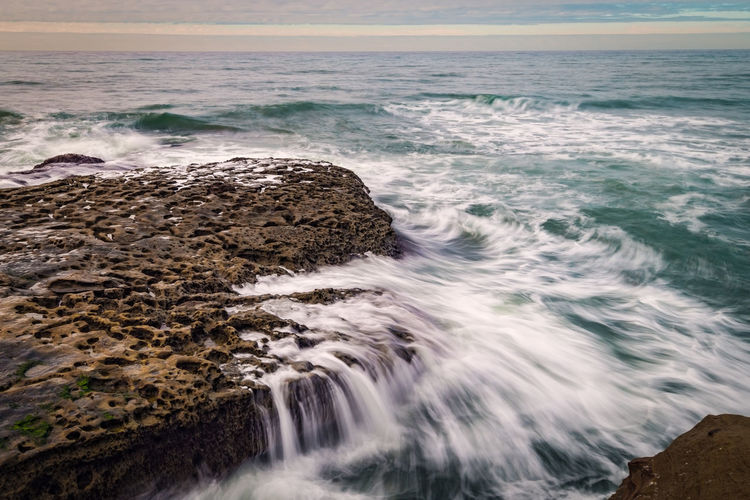 Long exposure surf crashing against beach bluffs on a cloudy day