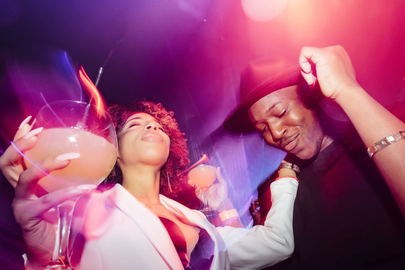 Drunk african american couple dancing under bright neon light while having fun during party