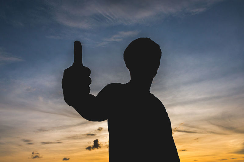 Silhouette man gesturing thumbs up against sky during sunset
