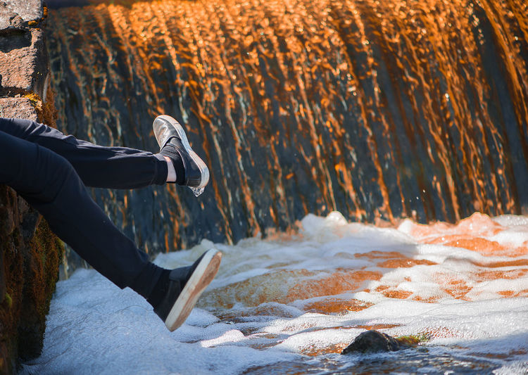 Low section of person sitting on rock over water