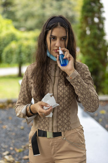 Teenager girl using nose inhaler in park. teen girl having pollen allergy