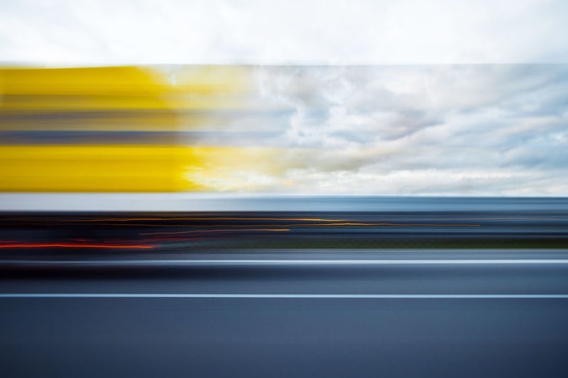 Blurred motion of yellow car against sky seen through glass window
