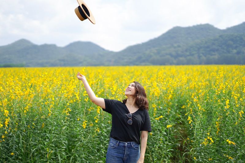 Full length of woman throwing hat in air while standing on field