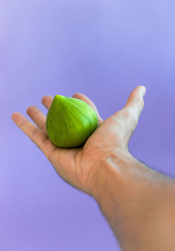 Cropped image of hand holding apple against blue background