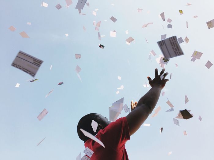 Low angle view of man with papers falling against sky