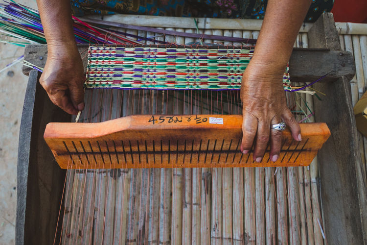 High angle view of cropped hands weaving loom